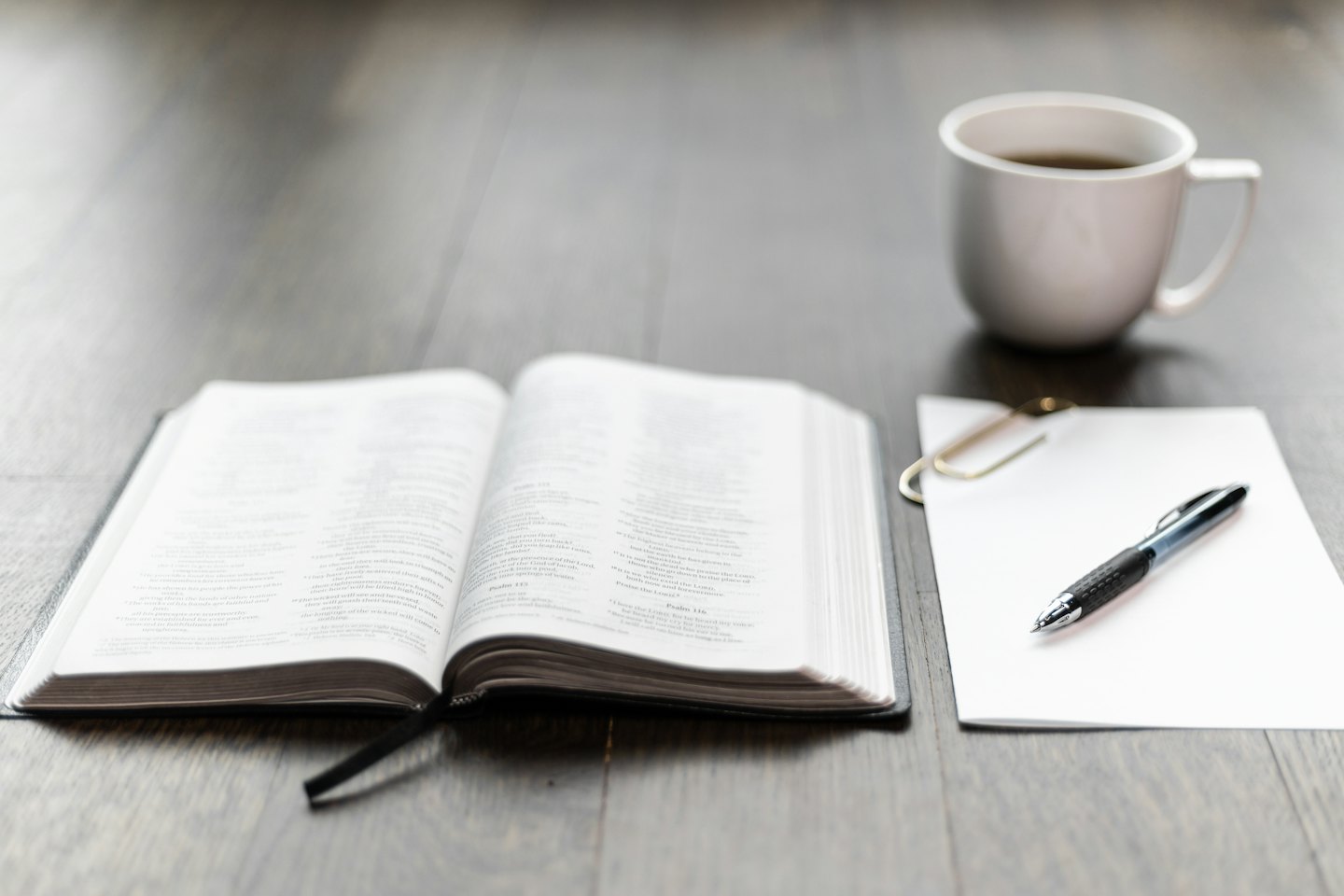 Open book, blank paper, pen, and coffee on a desk.