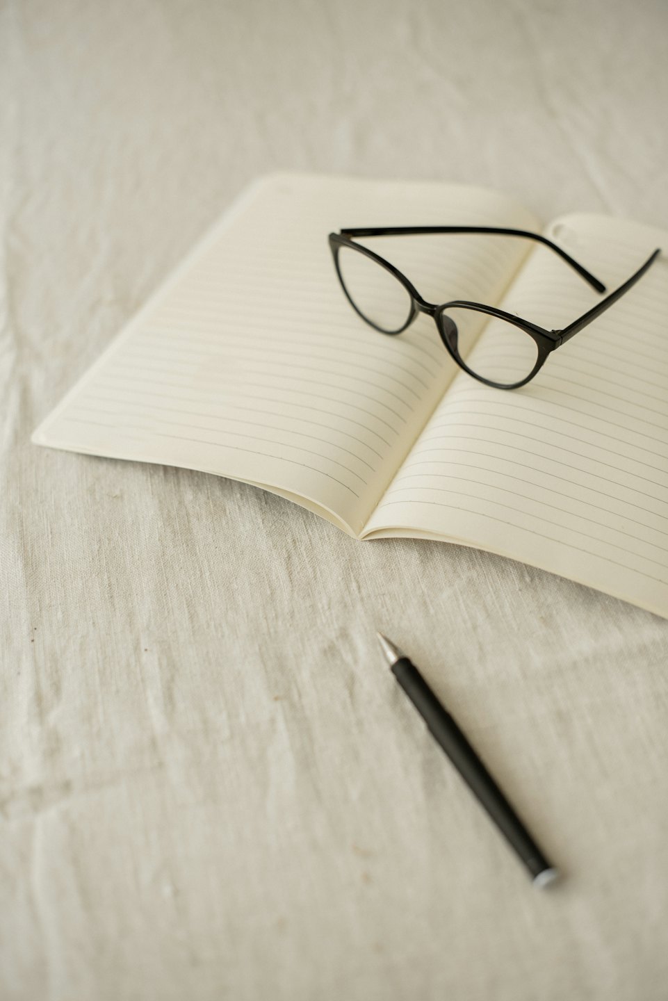 Notebook with reading glasses and pen on a fabric surface.